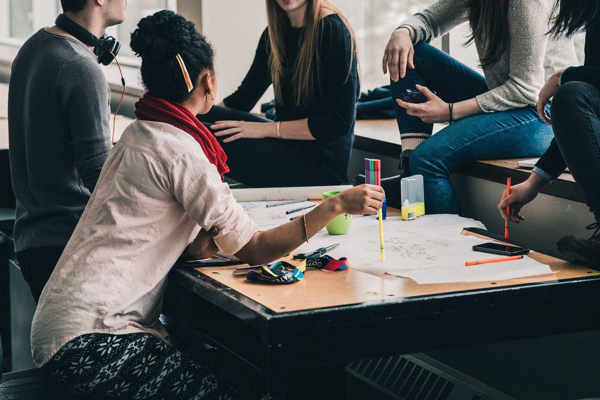 Quelle: pixabay.com / Stocksnap, https://pixabay.com/de/photos/menschen-m%c3%a4dchen-frauen-studenten-2557396/ junge Gruppe berät sich an Tisch